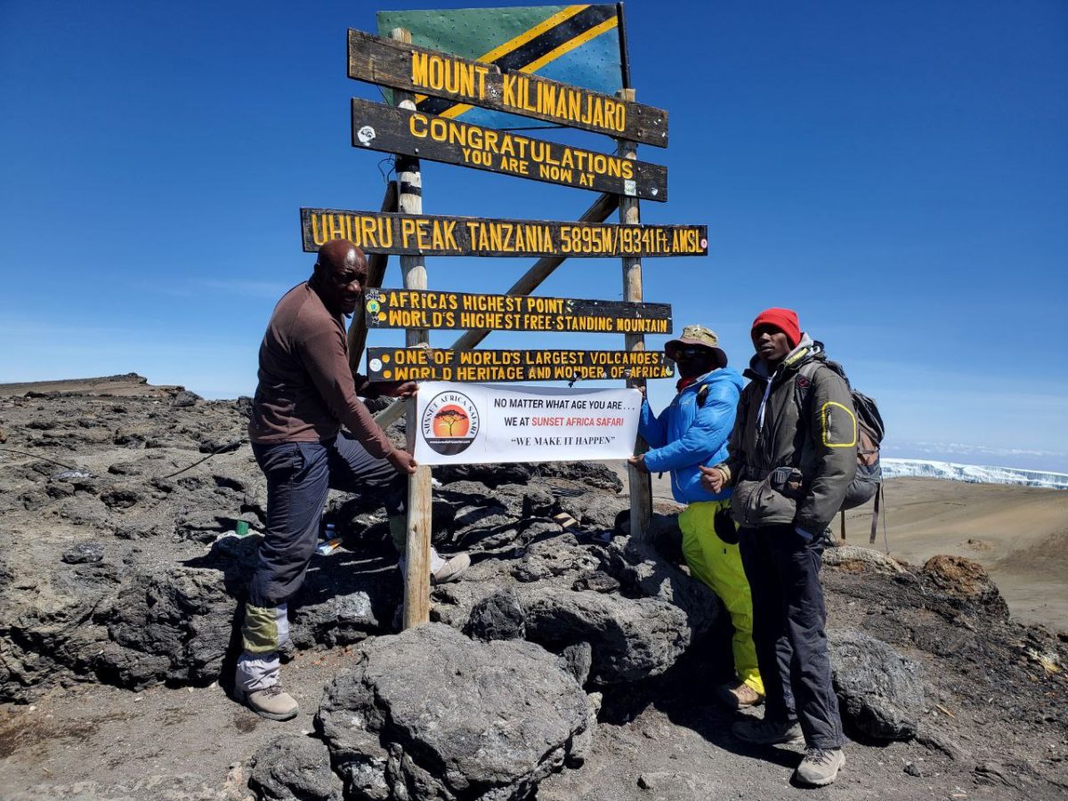 Climbers holding a Sunset Africa Safari banner at the Uhuru Peak sign on Kilimanjaro, 5,895 m