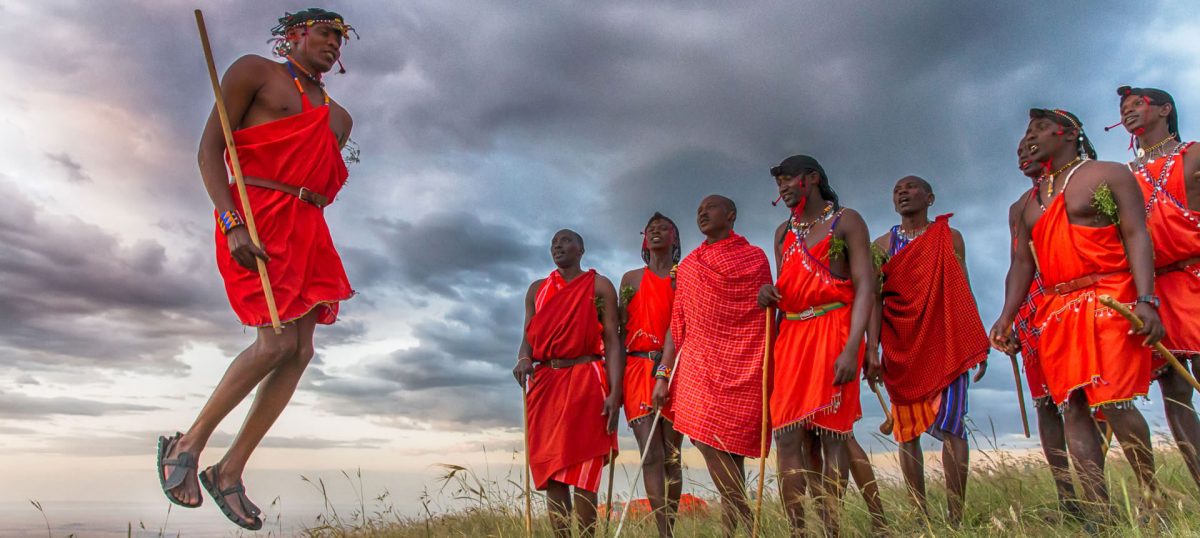 Maasai men in red shukas doing the jumping dance under a cloudy sky